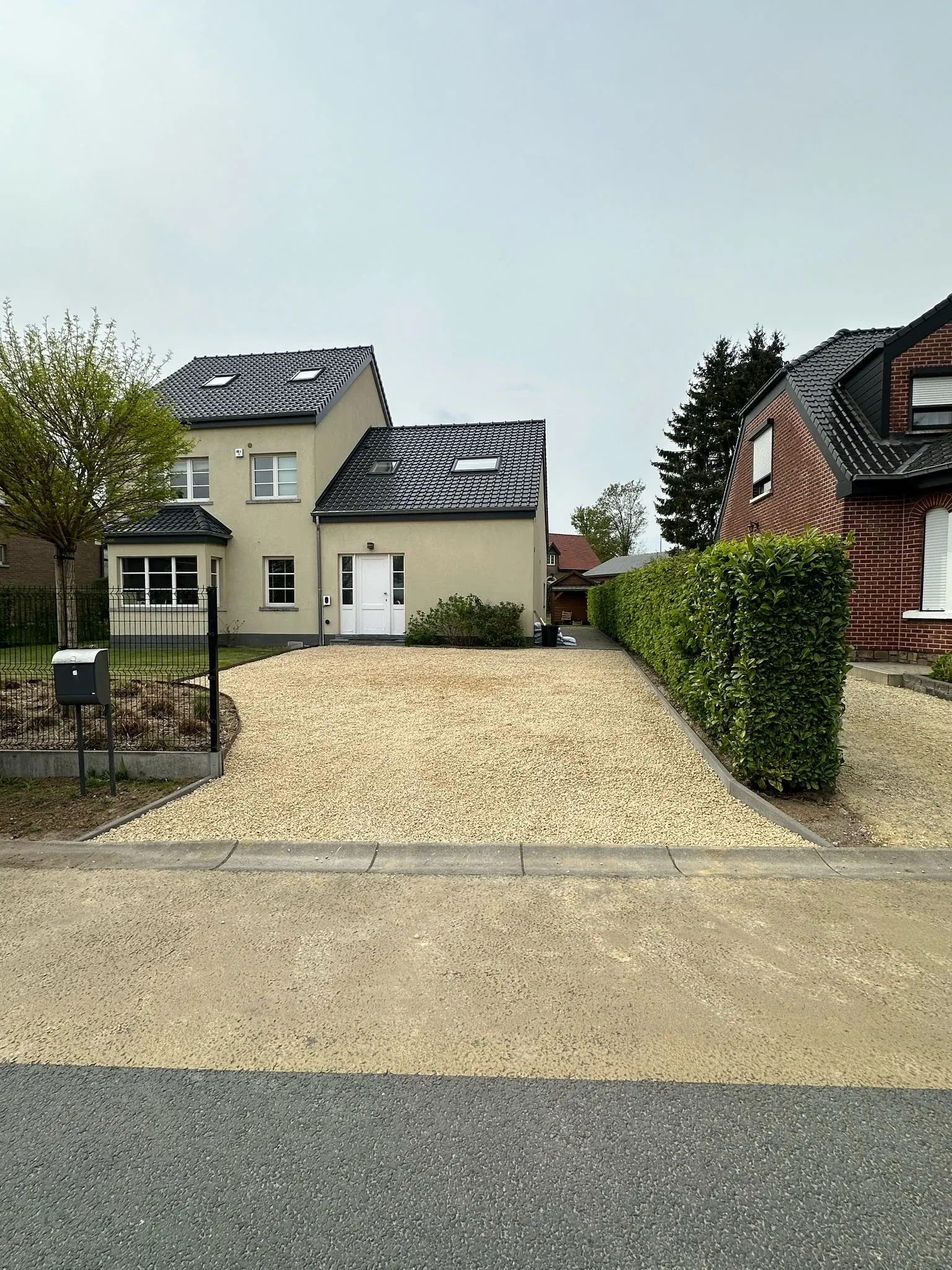 Na: oprit in beige steenslag met betonnen boordstenen voor de woning