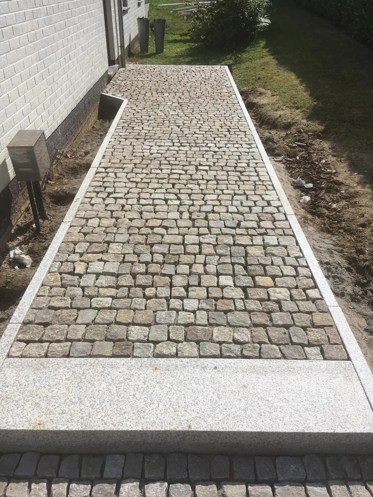 Chemin en pavés de pierre naturelle bordé de granit clair le long d’une maison