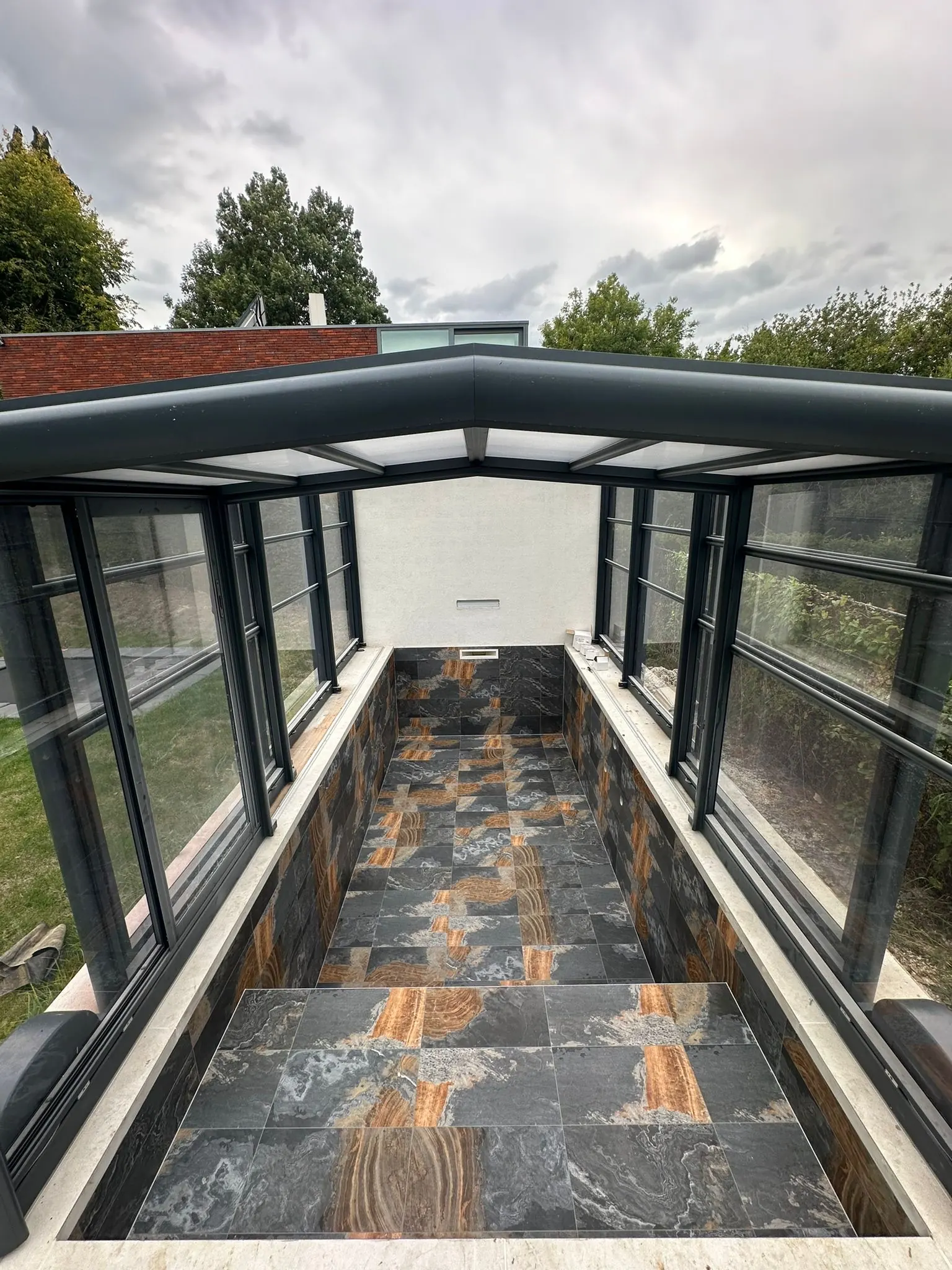 Piscine carrelée en gris ardoise veiné d’orange, sous un abri vitré