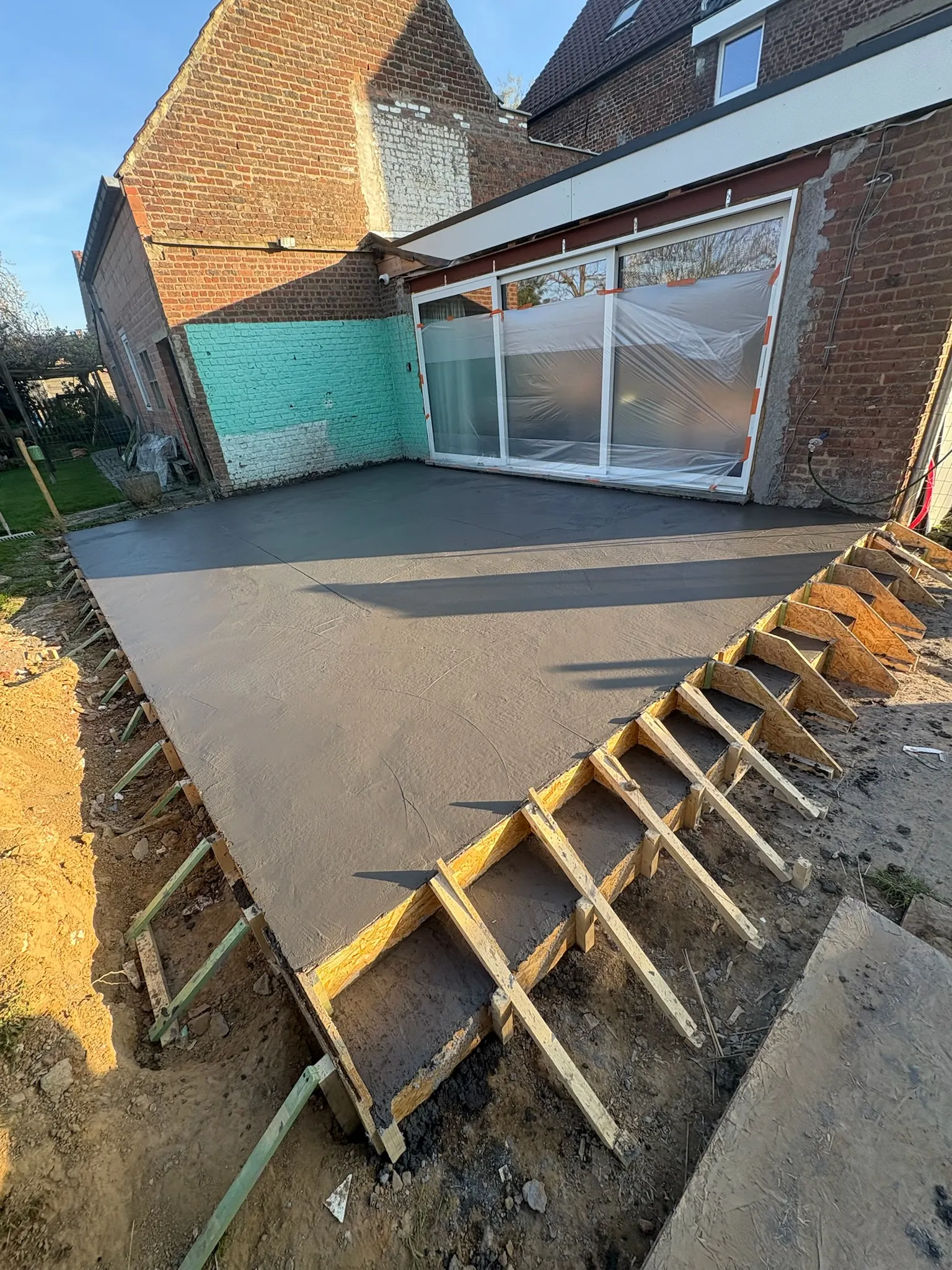 Dalle de terrasse en béton frais devant une extension vitrée, coffrage bois des marches