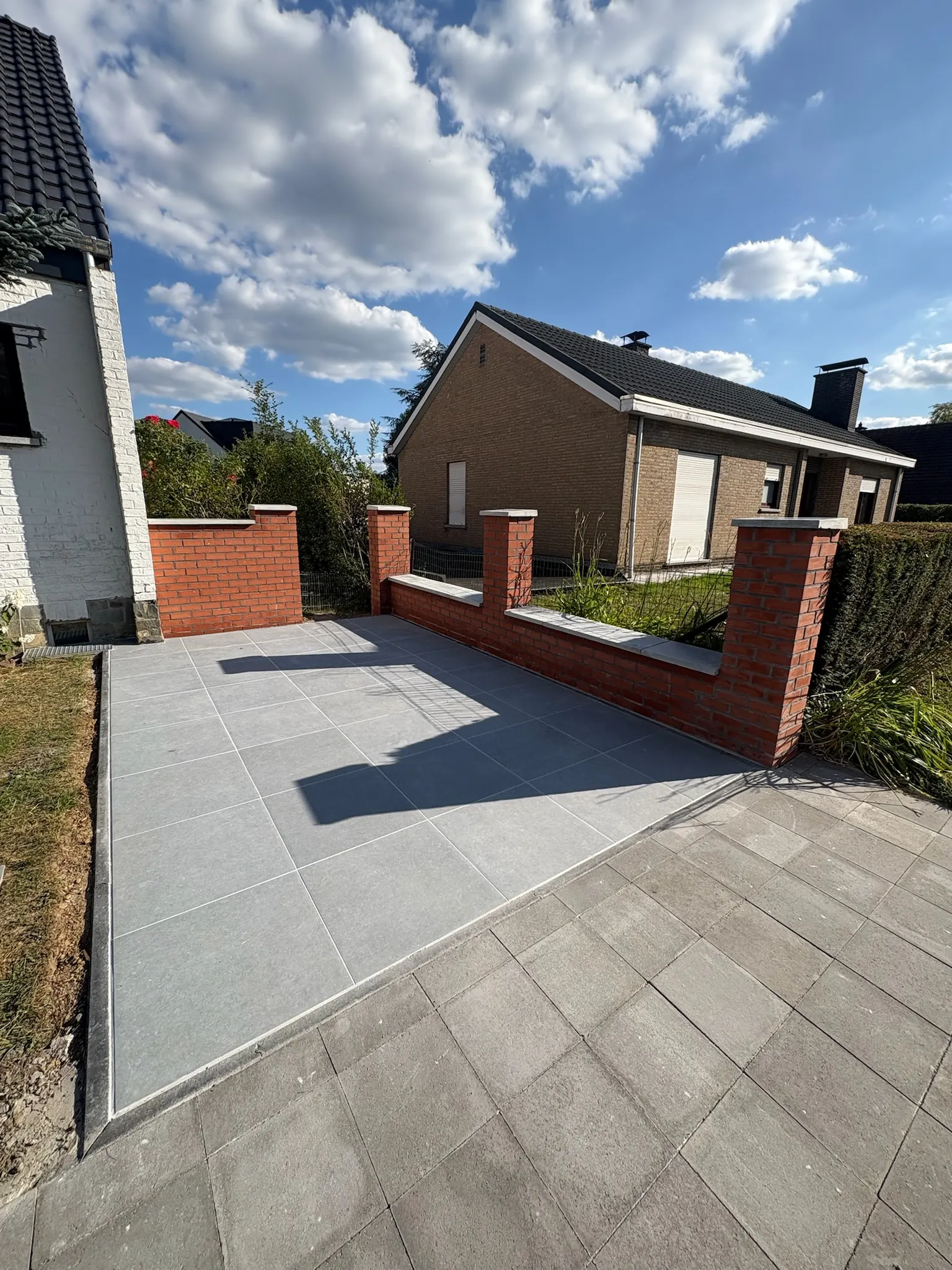 Terrasse en dalles grises entourée d’un muret de briques rouges à piliers
